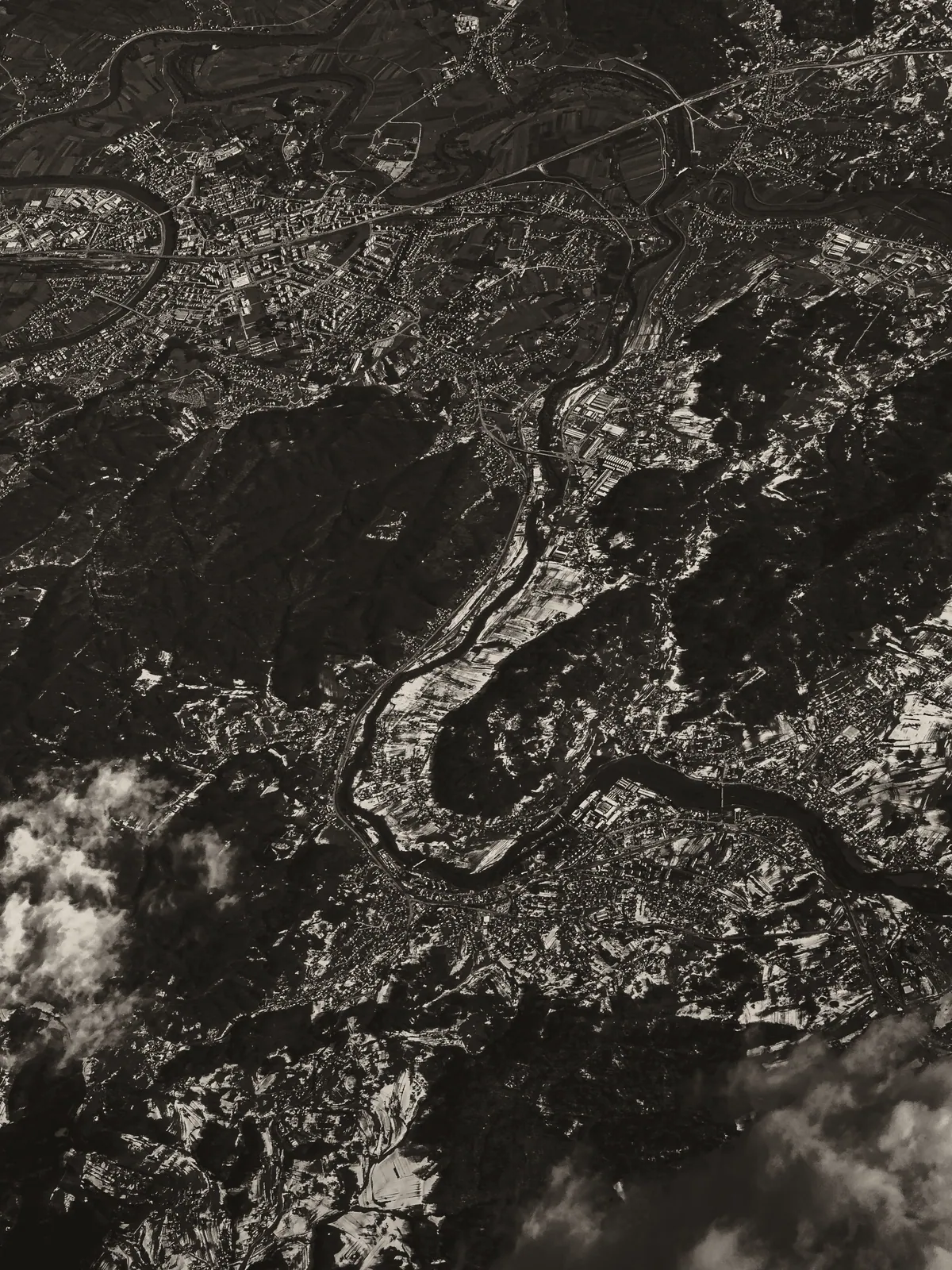 Aerial view of terrain cut by a winding river, in warm monochrome