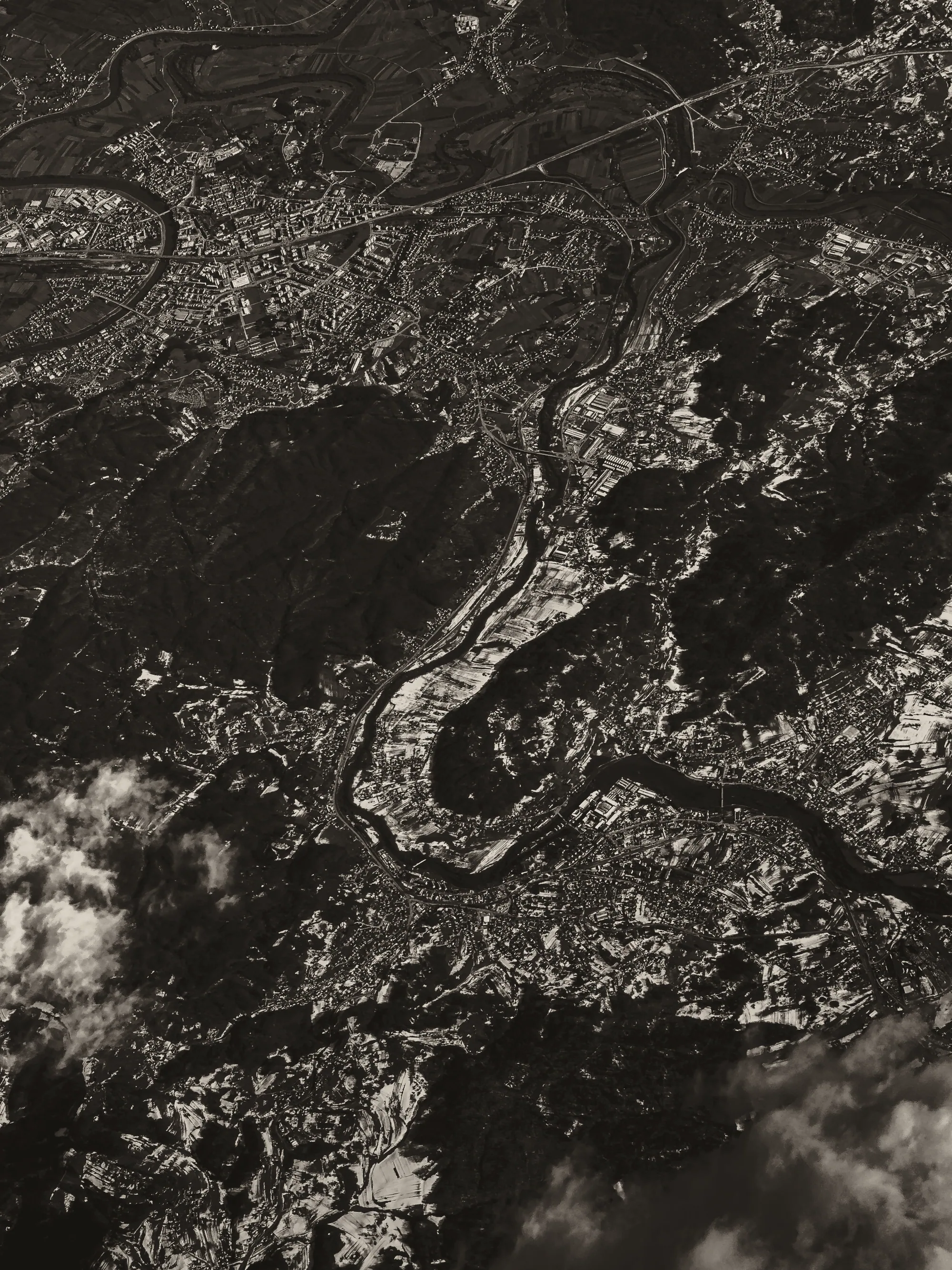 Aerial view of terrain cut by a winding river, in warm monochrome